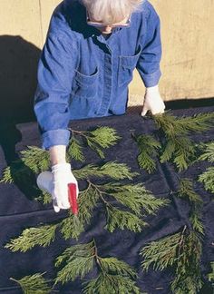 a woman in blue shirt and white gloves working on a piece of wood with pine needles