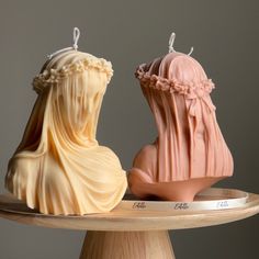 two small candles sitting on top of a wooden table next to each other in the shape of women's heads