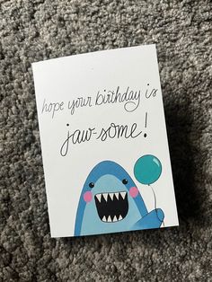 a birthday card with a cartoon shark holding a balloon and saying, hope your birthday is jaw -some