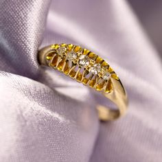 a gold ring with three diamonds on it sitting on a purple satin surface, surrounded by white and yellow fabric