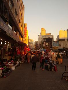 people are walking through an outdoor market with christmas decorations and lights on the buildings in the background