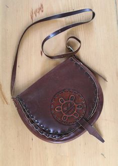 "Amazing hand tooled leather crossbody bag or shoulder bag from the 60's, possibly 70's in a rare mahogany color. Long adjustable strap. *Measurements:  Approximately 9\" high x 11\" wide (at widest)  Straps: drops about 22\" at longest *Condition: Good condition for age. *Note - Some scratches and marks throughout. Black lines on back and front. Inside is fairly clean. *All items listed here are vintage and pre-owned (unless otherwise noted), which means they will likely have some wear, including stains or scratches. I will call out any major imperfections but purchasing vintage means buying items that have been previously loved and used. Please reach out with any questions before buying as I'm happy to provide any additional information and photos to help you in your purchasing decision. Vintage Brown Crossbody Saddle Bag, Vintage Brown Saddle Bag With Leather Backing, Vintage Brown Saddle Shoulder Bag, Retro Brown Hand Tooled Shoulder Bag, Retro Vintage Brown Hand Tooled Shoulder Bag, Brown Retro Shoulder Bag With Hand Tooled Details, Retro Brown Hand-tooled Satchel, Hand-tooled Brown Crossbody Satchel, Vintage Brown Hand Tooled Crossbody Shoulder Bag