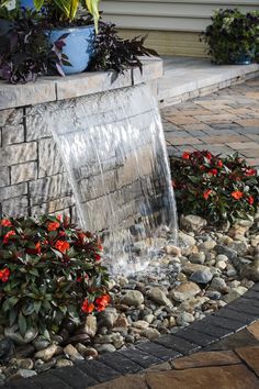 a water fountain in the middle of a garden with red flowers growing out of it