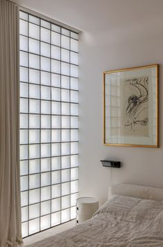 a white bed sitting next to a window in a bedroom under a framed art piece