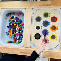 a child is playing with an art box filled with colorful beads and wooden trays