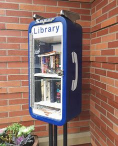 a blue and white book vending machine sitting in front of a brick wall next to a potted plant