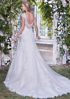 a woman in a wedding dress is standing under an arch with white flowers on it