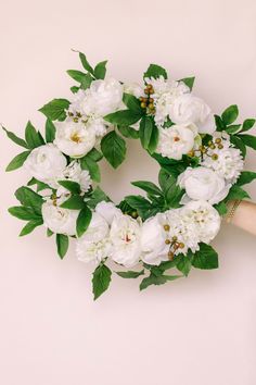 white flowers and green leaves are arranged in a wreath