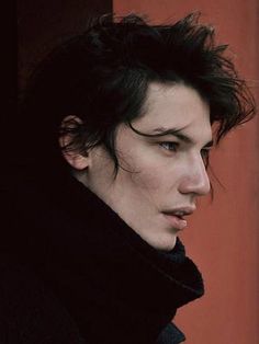 a young man with black hair is looking at something in the distance while wearing a coat