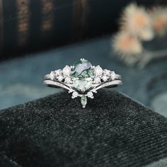 an engagement ring with green and white stones on the front, sitting on a black velvet box