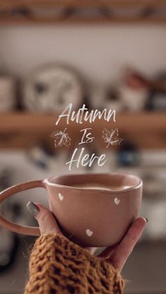 someone holding a cup with the words autumn is here