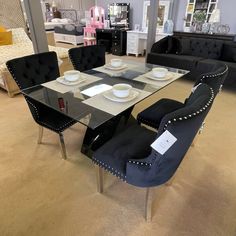 a glass table with black chairs and plates on it in a room filled with furniture