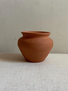 a brown vase sitting on top of a white tablecloth covered floor next to a wall