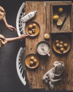 two people sitting at a wooden table with plates and bowls of food on the table