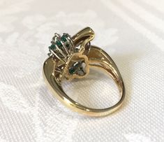 Emerald and diamond cluster ring. 14K yellow gold statement ring has 14 round vibrant green genuine emeralds, & 10 round shimmering diamonds in a free form design across the top of the ring. Below the gemstones is a detailed open airy under gallery. The design is like a bow with the ends being all high polished yellow gold. There is a beautiful rounded shank that tapers on the bottom to 2.5mm. Ring is a size 7 1/2 and can be resized 14 Emeralds app. .75cts have intense green color 10 Diamond Green Emerald-cut Cluster Ring With Diamond Accents, Emerald Cut Green Cluster Ring With Diamond Accents, Classic Green Cluster Diamond Ring, Green Cluster Diamond Ring For Anniversary, Emerald Cluster Ring With Diamonds, Green Emerald Cluster Ring With Diamonds, Green Emerald Cluster Ring With Brilliant Cut, Green Cluster Jewelry With Diamond Accents, Heirloom Green Cluster Ring