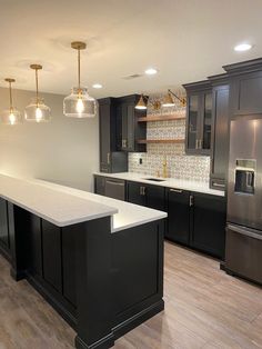 an empty kitchen with black cabinets and white counter tops is pictured in this image, there are lights hanging from the ceiling