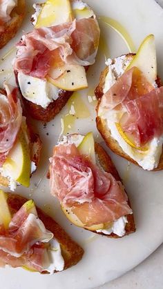 several pieces of bread topped with prosciutto and other toppings on a white plate