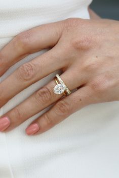 a woman's hand wearing a gold ring with a diamond in the middle and a white dress underneath