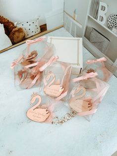 five pink swan shaped cookies in clear boxes on a white countertop next to a teddy bear