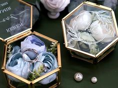 two wedding rings are sitting in an octagonal box with flowers and pearls on the table