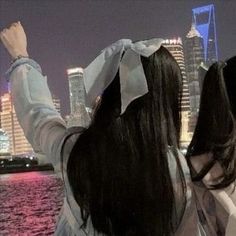 two women standing next to each other in front of a body of water at night