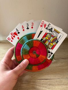 a hand holding four playing cards in front of a deck of cards on top of a wooden table