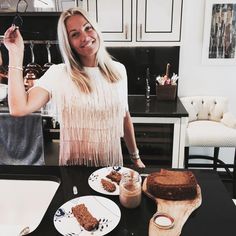 a woman standing in front of a table with cake on it and coffee mugs next to her