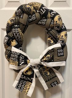 a black and gold saints wreath on a door with white ribbon hanging from the front