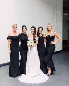 four bridesmaids in black dresses posing for a photo outside the building with their bouquets