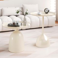 two white tables sitting on top of a carpeted floor next to a living room couch