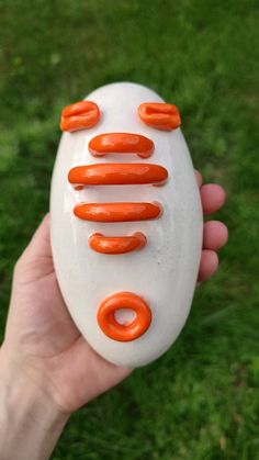 a hand holding an orange and white object in it's left hand, with several circles painted on the top