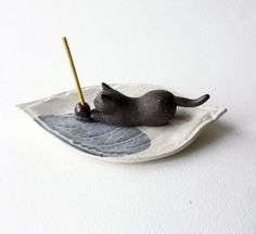 a cat figurine laying on top of a plate with a stick in it