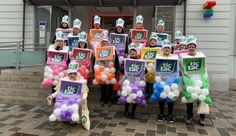 a group of people standing in front of a building with balloons and signs on their heads