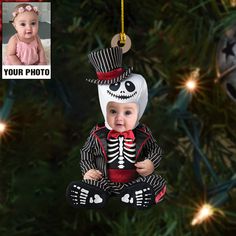 a baby wearing a skeleton costume sitting in front of a christmas tree with a photo hanging from it