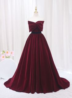 Accentuate your elegance in this stunning burgundy prom dress! Crafted from luxurious velvet, this gown exudes sophistication with its deep red hue and sumptuous texture. The bodice features a unique bow-like detail at the neckline, creating a striking focal point that is both modern and chic. The waist is cinched with a sleek black band, enhancing the natural silhouette and leading to a full, flowing skirt that gracefully sweeps the floor as you move. Perfect for a prom or a formal evening event, this dress is designed to make a bold statement. Its timeless color and refined design ensure you will turn heads, while its classic cut provides comfort and style in equal measure. Bow Prom Dress, Princess Prom Dress, Prom Dress Burgundy, Burgundy Prom, Princess Prom Dresses, Velvet Prom Dress, Strapless Prom Dress, Prom Dress Plus Size, Plus Size Prom