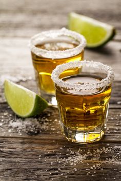 two shot glasses filled with ice and limes on top of a wooden table covered in sugar