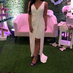 a woman standing in front of a pink couch wearing a white dress and blue heels