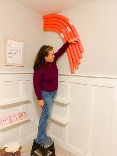 a woman standing on top of a step stool holding an orange object above her head