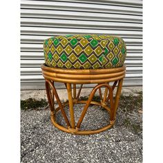 a bamboo stool with a green and yellow cushion sitting on gravel next to a building