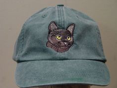 a green hat with a black cat embroidered on the front and yellow eyes behind it