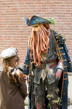 two people standing next to each other in front of a brick wall with a statue of a pirate