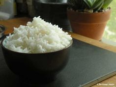 a bowl filled with white rice sitting on top of a table next to a potted plant