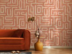 an orange couch sitting in front of a wall with a pattern on it and a vase next to it