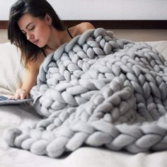 a woman laying in bed with a blanket on top of her and reading a book