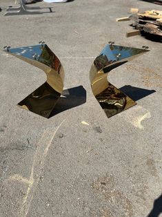 two shiny metal sculptures sitting on top of a cement ground next to a pile of wood