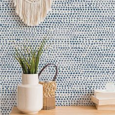 a white vase sitting on top of a wooden table next to a wallpapered wall