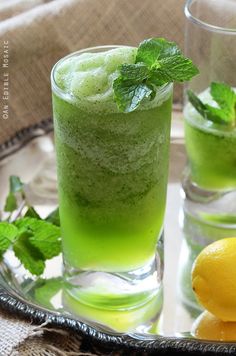 two glasses filled with green drinks on top of a table