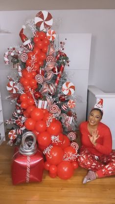 a woman sitting on the floor next to a christmas tree with candy canes all over it