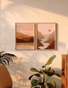 two paintings hanging on the wall next to a plant in a living room with a couch