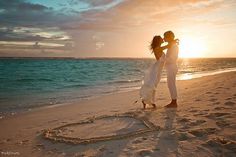 two people are standing on the beach with their arms around each other as the sun sets behind them